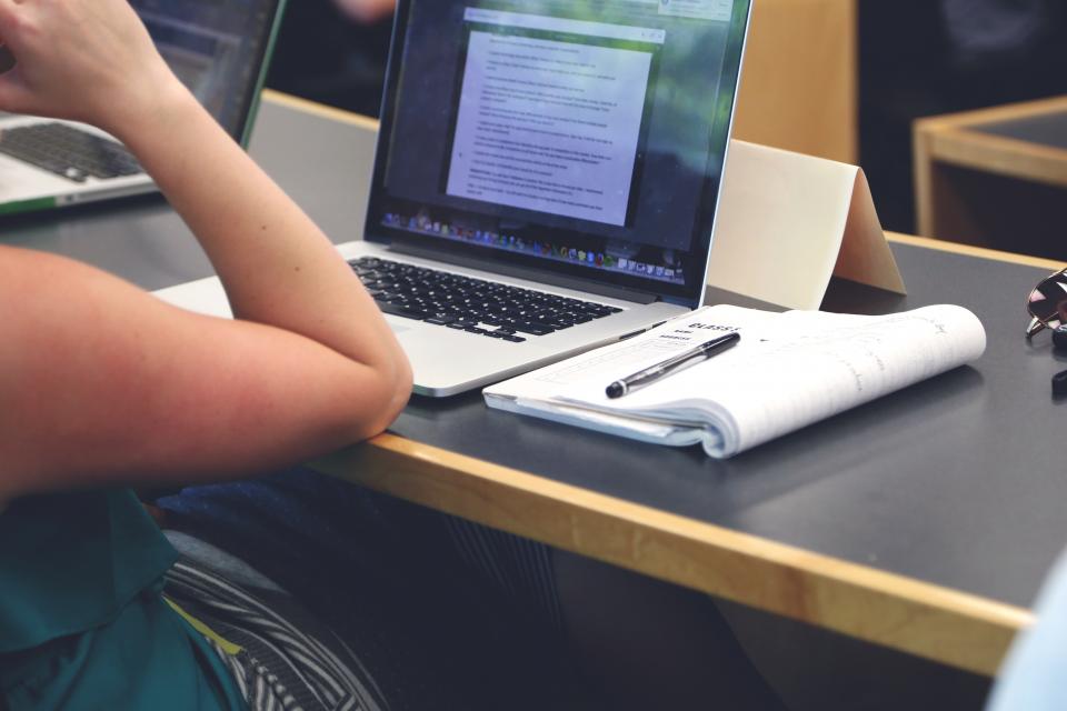 Laptop és jegyzetfüzet egy asztalon, feladatmegoldás közben