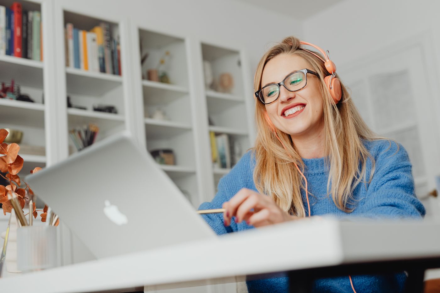 Mosolygó, szemüveges egyetemista lány kék pulóverben a laptopja előtt